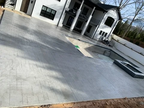 Wide stamped concrete patio behind a white house with a pool